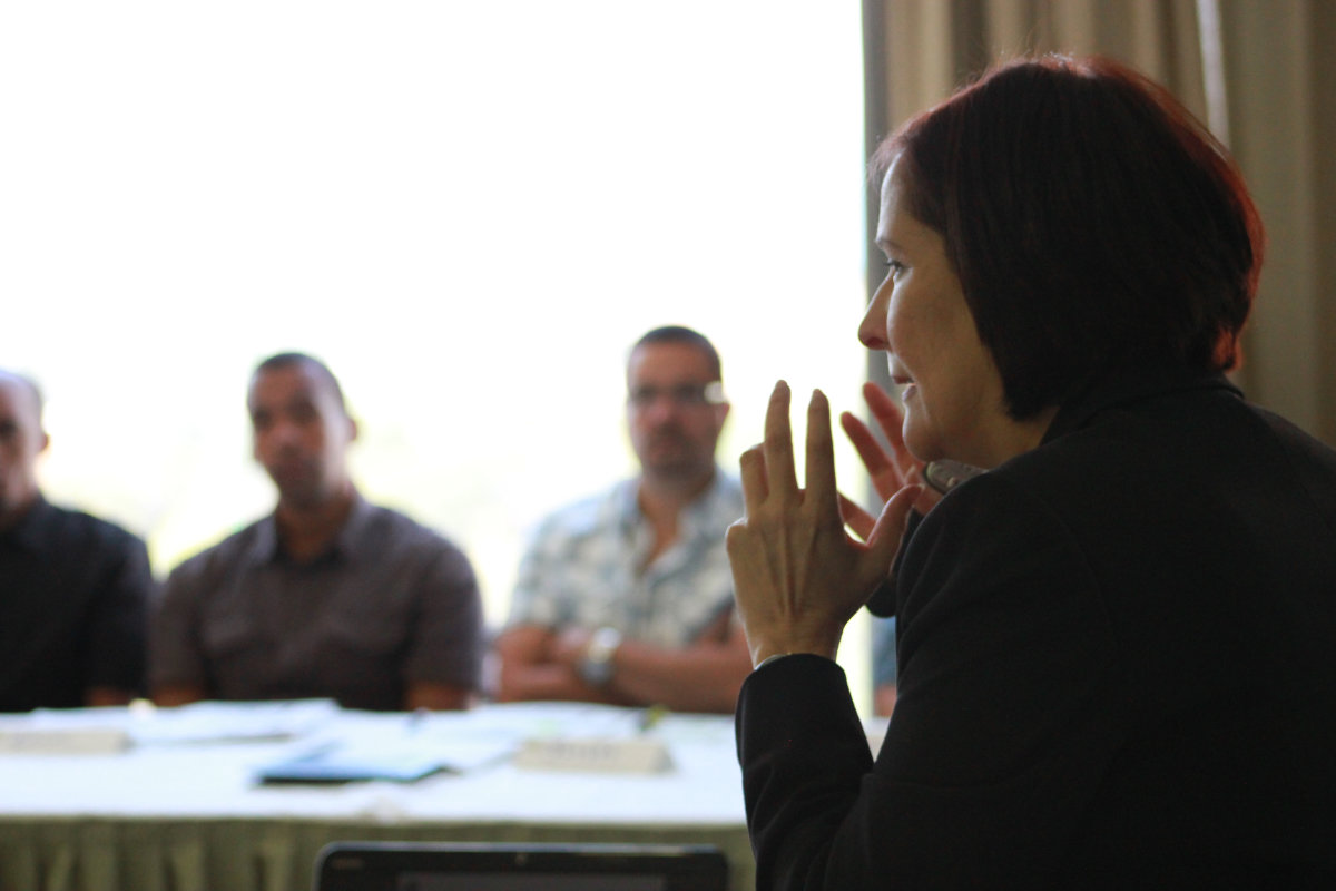 Foto de perfil del rostro de una instructora de Suprema Qualitas haciendo gestos con sus manos mientras imparte un curso a un grupo de personas.