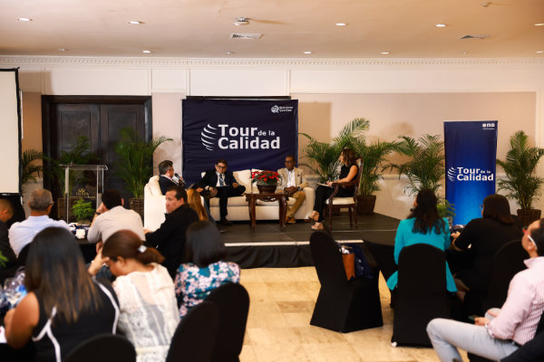 Foto con un escenario de panelistas de expertos al fondo y un grupo de personas escuchando a los panelistas.